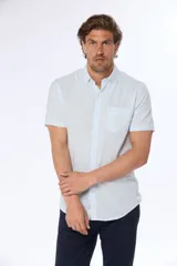 Camisa celeste y blanca a rayas verticales, de lino y algodón, manga corta, corte slim fit, con cuello abotonado y bolsillo en el pecho.