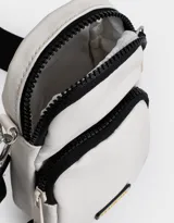 Bandolera color crudo con detalles en negro, correa ancha regulable y bolsillo frontal.