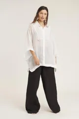 Camisa blanca de lino con corte amplio, cuello camisero y mangas 3/4 con detalle de puntilla en el borde.