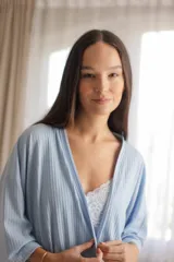 Bata tipo kimono de algodón color blanco hueso, con textura acanalada vertical. Presenta un cruce frontal asegurado con un lazo a la cintura y mangas anchas de largo al codo.