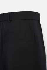 Pantalón negro de corte amplio confeccionado en tejido con mezcla de viscosa. Presenta cintura elástica, pliegues en la parte delantera, bolsillos laterales y traseros de vivo. Cierre frontal con cremallera y gancho metálico oculto.