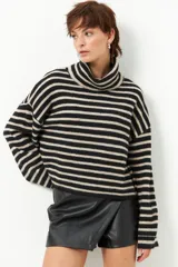 Polera de punto a rayas en tonos negro y crema, con cuello alto y diseño holgado, confeccionada en poliéster reciclado.