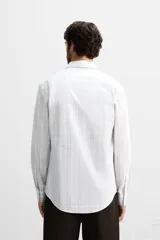 Camisa de vestir slim fit de algodón, color blanco con diseño de cuadros en tonos grises y beige. Tiene cuello italiano, mangas largas con puños abotonados y cierre frontal con botones.