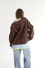 Buzo celeste con cuello polo y puños en rib color verde lima. Tiene un parche con el logo de la marca en el pecho y rayas horizontales en el ruedo.