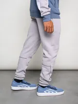 Pantalón de jogging gris claro, corte clásico, con logo de la marca Umbro bordado en negro en el muslo izquierdo y costuras en contraste.