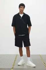 Short cargo negro de popelina de algodón, con cintura elástica ajustable con cordón, bolsillos laterales, bolsillos cargo con solapa y botón a presión en piernas y traseros, y aberturas laterales en el bajo.