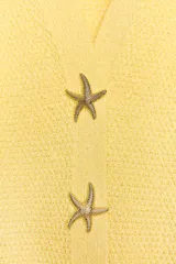 Chaqueta amarilla de punto con escote de pico y manga corta. Cierre frontal con botones en forma de estrella.