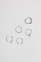 Set de anillos plateados con diferentes diseños: uno liso con una piedra, uno con una hilera de pequeñas piedras, uno con forma de estrella, uno con diseño trenzado y uno con pequeñas piedras incrustadas.