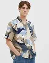 Camisa de manga corta con cuello resort y cierre de botones. Confeccionada en tejido plano de viscosa LENZING™ ECOVERO™ con estampado abstracto en tonos beige, azul y gris.