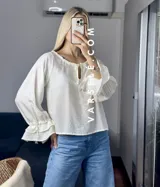 Blusa blanca de mangas largas con volados en los puños y escote con lazo.