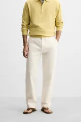 Pantalón chino color crema de corte recto, confeccionado en tejido de algodón con elasticidad. Cuenta con bolsillos frontales y traseros de plastrón con botón. Cierre frontal con cremallera y botón.