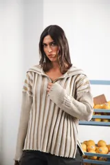 Buzo color beige con rayas horizontales en lurex dorado, cuello con medio cierre, corte oversized y logo tejido en el puño.