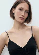 Vestido largo negro de corte recto, con escote de pico y detalle de lazo en el centro del busto. Presenta tirantes finos y no tiene cierre.