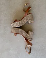 Sandalias de plataforma con capellada de cuero color marrón, tobillera con hebilla dorada y base de rafia.