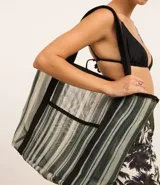 Bolso de playa rectangular de poliéster con rayas verticales en tonos de verde, gris y blanco. Tiene asas de algodón negras y un bolsillo externo.