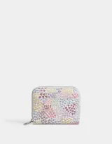 Billetera de cuerina color blanco con estampado de flores en tonos lila, naranja y amarillo. Tiene cierre superior, compartimentos para tarjetas y billetes, y un bolsillo interno con cierre.