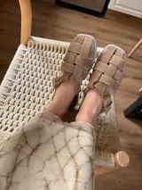 Sandalias de cuero marrón con diseño de tiras entretejidas y hebilla lateral.
