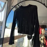 Top negro de tul transparente con cuello alto y mangas largas acampanadas.