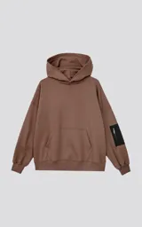 Buzo hoodie marrón de corte oversize, confeccionado en algodón rústico. Tiene capucha forrada, bolsillo tipo bomber con cierre en la manga y bolsillo canguro.