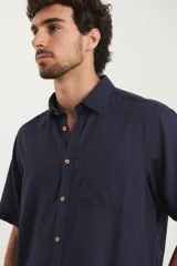 Camisa sport de manga corta color verde oliva, línea premium, con cuello clásico, cierre frontal con botones de coco y bolsillo de parche en el pecho. Confeccionada en lino y algodón.