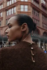 Vestido midi de manga larga, color marrón oscuro, confeccionado en tejido de encaje o punto con patrón floral sutil. Presenta cuello perkins y drapeado asimétrico en el torso con frunces laterales.