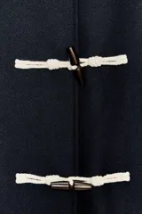 Abrigo azul marino de lana con cuello solapa, manga larga con trabillas y bolsillos de plastrón. Cierre frontal con alamares a contraste.
