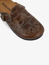 Mules de cuero color marrón con diseño vaquero, costuras decorativas con forma de águila y hebilla lateral ajustable.
