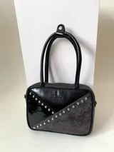 Cartera rígida negra de cuero con tachas plateadas y tres combinaciones de cuero diferentes que aportan textura. Tiene herrajes y cierre metálico plateado marca YKK. Cuenta con un asa fina para llevar al hombro o en la mano y una correa larga extra regulable.