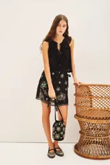 Falda corta cruzada forrada, color negro, con lazo lateral y bordados florales en frente y espalda.