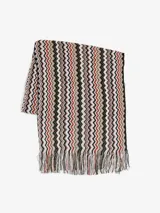 Poncho tejido de punto con diseño zigzag multicolor en tonos blanco, negro, marrón y rojo. Tiene flecos en los bordes.