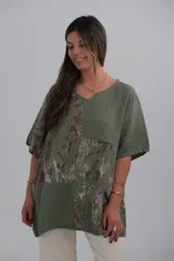 Blusa verde militar con estampado de hojas en tonos marrones y blancos, cuello en V y mangas cortas.