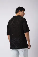 Camisa negra tejida de manga corta, con calado aireado, cuello tipo bowling y botones al tono. Diseño de corte relajado.
