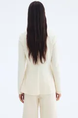 Blazer entallado color crema, de punto interlock pesado con cuello redondo y botones forrados hasta la cintura, creando un leve corte acampanado.