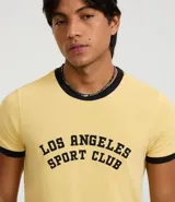 Remera de manga corta estilo ringer, color amarillo claro con ribetes negros en cuello y mangas. Presenta un estampado central en negro con el texto "Los Angeles Sport Club".