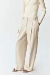 Pantalón de vestir color crema, de tiro alto y pernera ancha, con pinzas delanteras, bolsillos frontales y falsos bolsillos de doble vivo en la espalda.