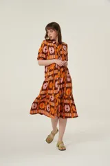 Vestido midi con estampado abstracto en tonos marrón, naranja y rosa. Tiene cuello camisero, mangas cortas abullonadas y falda escalonada con volantes.