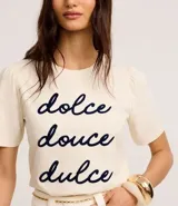 Remera color crema de algodón con cuello redondo y mangas cortas abullonadas. Estampa frontal con la frase "dolce douce dulce" en letras cursivas azul marino.