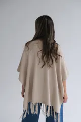 Ruana color beige de tejido de punto con flecos en el ruedo.