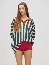 Chomba de corte oversize con cuello camisero, a rayas verticales en color marrón, lila y blanco. Tiene un logo bordado en el pecho y puños en color marrón.