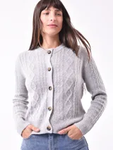 Cárdigan tejido color gris claro con diseño trenzado, cuello redondo y cierre frontal con botones marrones.