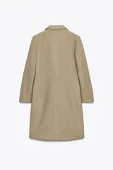 Abrigo largo color beige, de cuello solapa y manga larga con hombreras. Tiene bolsillos con solapa en la parte delantera y cierre frontal con botones.