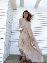 Vestido camisero largo color beige con rayas verticales blancas, cuello camisero, abotonadura frontal completa, mangas largas con puños abotonados y falda con volantes.