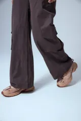 Pantalón cargo marrón de gabardina, con cierre metálico lateral, elástico en cintura trasera, recortes delanteros y bolsillos tipo cargo.