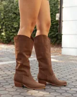 Botas texanas de caña media confeccionadas en cuero gamuzado color marrón. Presentan un diseño de corte clásico con costuras decorativas en el empeine, puntera levemente redondeada y taco bajo de madera.