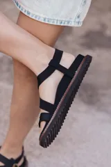 Sandalias planas color tostado con tiras cruzadas y hebillas doradas.