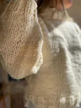 Sweater tejido de lana merino color crudo, con cuello alto y mangas largas abullonadas. Tejido artesanal con punto grueso.