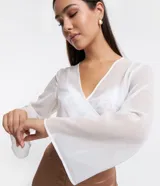 Blusa cropped de chiffon color blanco, con escote en V cruzado, mangas largas acampanadas y lazo en la espalda.