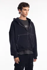 Campera negra con cierre frontal, capucha y costuras a la vista en color blanco. Tiene remaches metálicos y un pequeño bordado en el pecho.