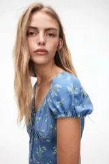 Vestido largo de lino y viscosa color celeste con estampado de flores blancas. Tiene mangas cortas abullonadas, escote corazón con tiras finas, copas preformadas con frunces, elástico en escote, hombros, mangas y cintura, cierre lateral oculto y tajo pronunciado en un lado.