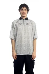Remera deportiva blanca con cuello polo negro, cierre parcial con cremallera, mangas cortas y estampado de letras grises.